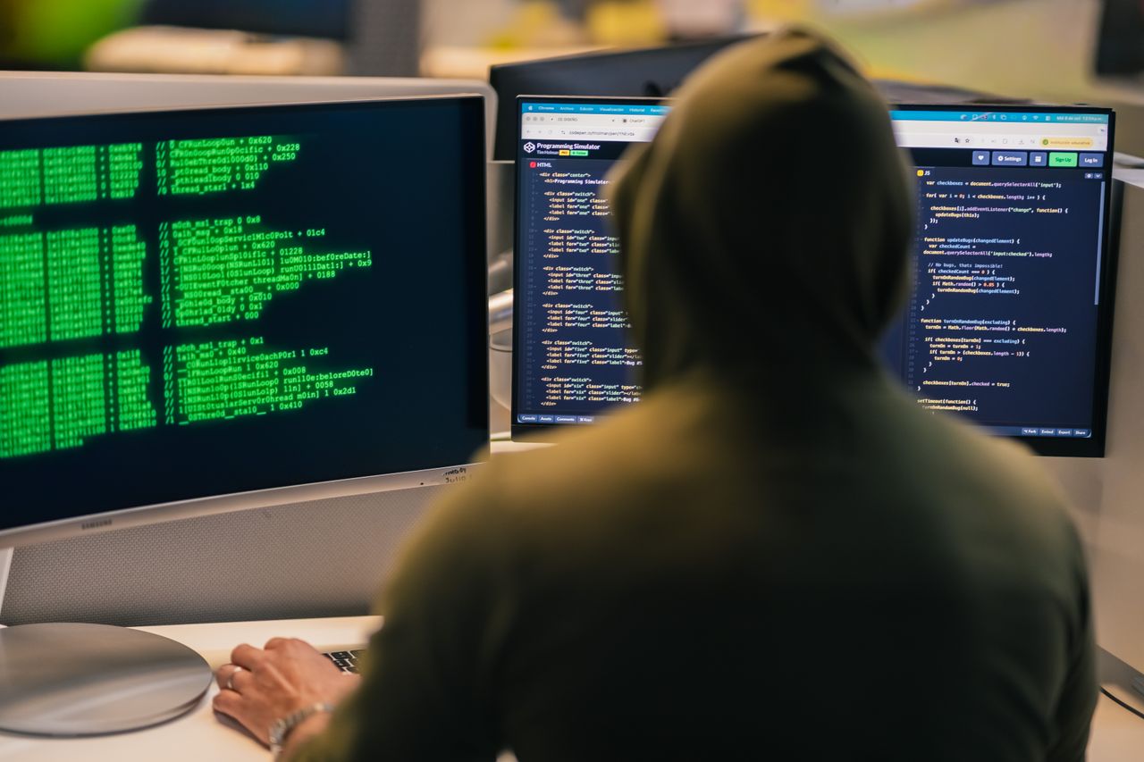 Crafting Captivating Headlines: Your awesome post title goes here A person in a hoodie coding on dual monitors, depicting cybersecurity and hacking themes.
