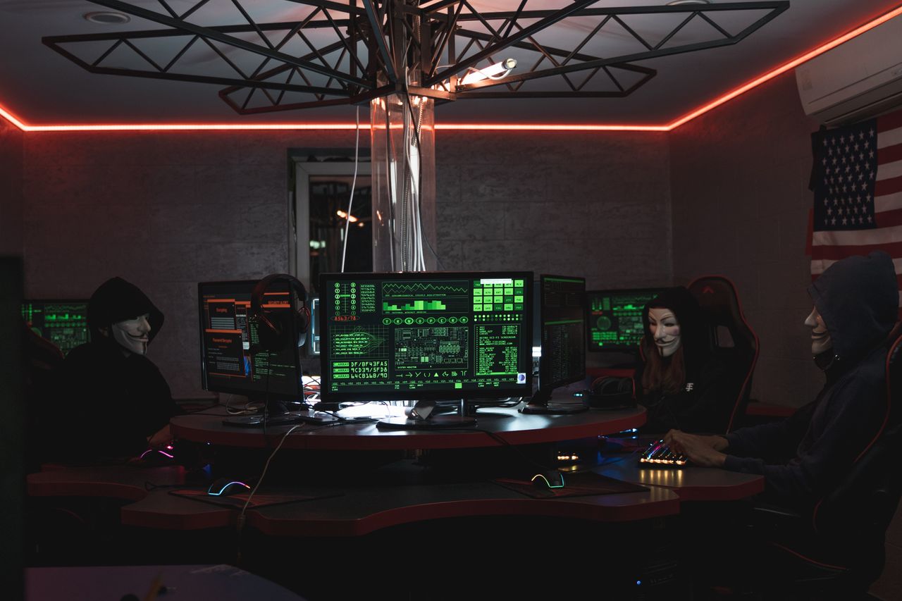 about-01 Team of hackers with Guy Fawkes masks coding in a dark room with computers.