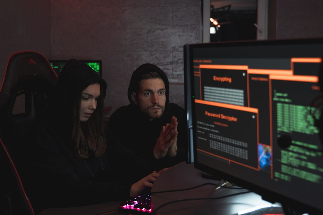 hero-01 Cybersecurity experts in hoodies analyzing encrypted data on computer screens in an indoor setting.