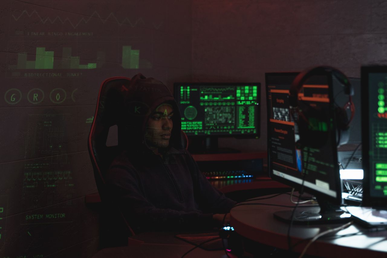 services-02 A man in a black hoodie engaged in cybersecurity work using multiple monitors indoors.