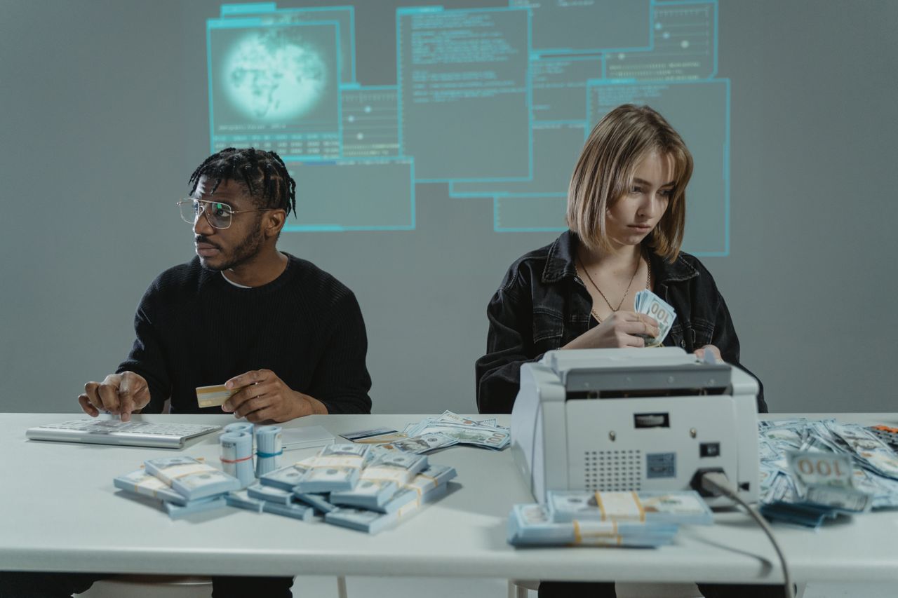 The Art of Drawing Readers In: Your attractive post title goes here Two individuals counting US dollar bills with a money machine, highlighting finance themes.